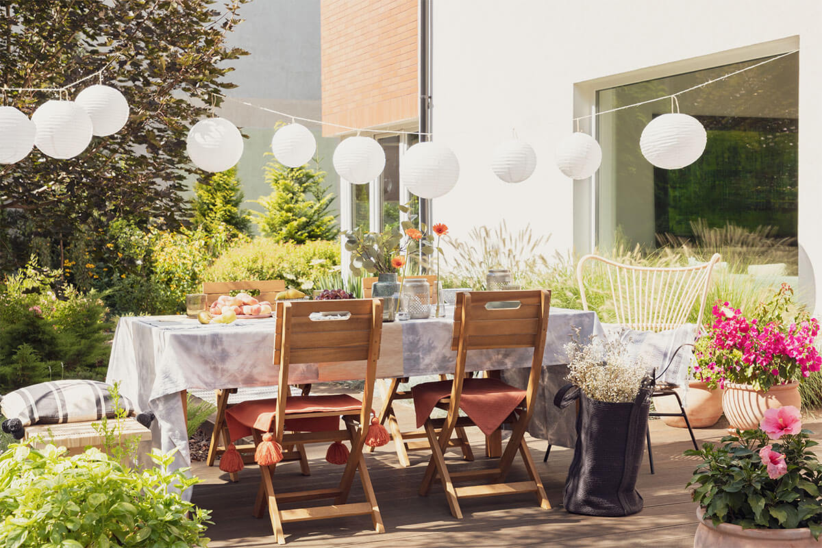 Markert GaLaBau - Terrassenbau - Holzterrasse vor dem Haus mit Möbeln, Pflanzen und Lampions